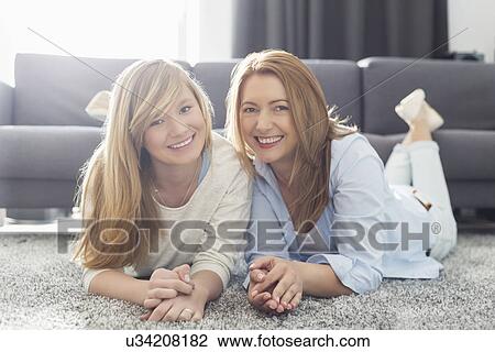 Stock Image - Portrait of smiling mother and daughter lying on carpet. Fotosearch