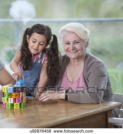 Stock Photo - Portrait of smiling senior woman with granddaughter playing with alphabet blocks at home. Fotosearch