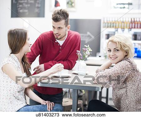 Stock Image - Portrait of smiling woman with friend at cafe table. Fotosearch