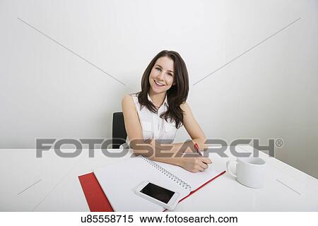 Portrait of smiling young businesswoman writing on binder at desk in office View Large Photo Image Stock Photography - Portrait of smiling young businesswoman writing on binder at desk in office. Fotosearch