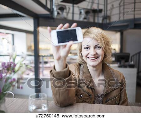 Portrait of smiling young woman displaying cell phone in cafe View Large Photo Image Stock Photography - Portrait of smiling young woman displaying cell phone in cafe. Fotosearch