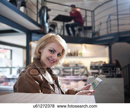 Stock Photo - Portrait of smiling young woman using tablet PC in cafe. Fotosearch