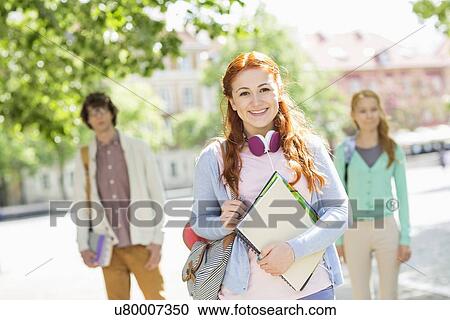 Stock Image - Portrait of young female student with friends in background on street. Fotosearch