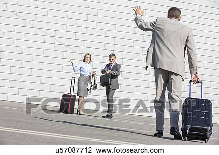 Rear view of businessman carrying luggage waving hand to colleagues View Large Photo Image Stock Image - Rear view of businessman carrying luggage waving hand to colleagues. Fotosearch