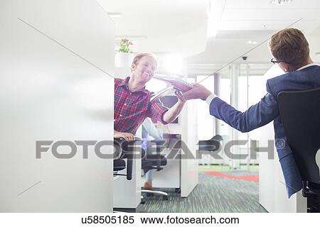 Stock Photography - Rear view of businessman giving files to colleague in creative office. Fotosearch