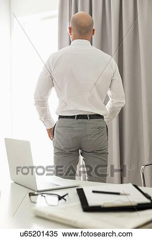 Rear view of businessman standing in home office View Large Photo Image Stock Photography - Rear view of businessman standing in home office. Fotosearch