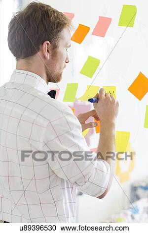 Rear view of businessman writing on sticky paper at creative office View Large Photo Image Stock Image - Rear view of businessman writing on sticky paper at creative office. Fotosearch