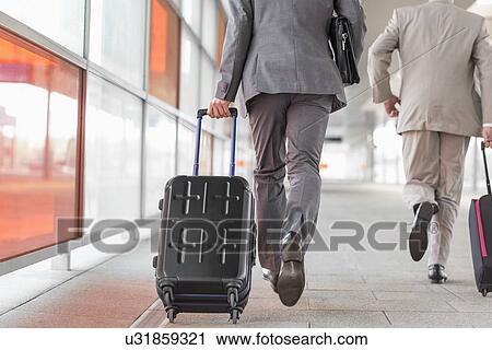 Stock Image - Rear view of businessmen with luggage running on railroad platform. Fotosearch
