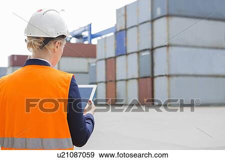 Rear view of female engineer using digital tablet in shipping yard View Large Photo Image Stock Photo - Rear view of female engineer using digital tablet in shipping yard. Fotosearch