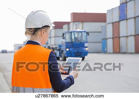 Stock Photography - Rear view of female engineer using tablet PC in shipping yard. Fotosearch