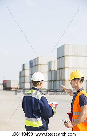 Rear view of male workers discussing in shipping yard View Large Photo Image Stock Photo - Rear view of male workers discussing in shipping yard. Fotosearch