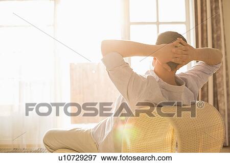Stock Photo - Rear view of man relaxing on chair at home. Fotosearch