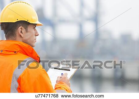 Rear view of mid adult man writing on clipboard in shipping yard View Large Photo Image Stock Photo - Rear view of mid adult man writing on clipboard in shipping yard. Fotosearch