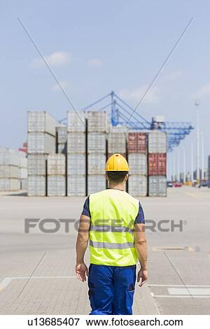 Rear view of mid adult worker walking in shipping yard View Large Photo Image Stock Photo - Rear view of mid adult worker walking in shipping yard. Fotosearch