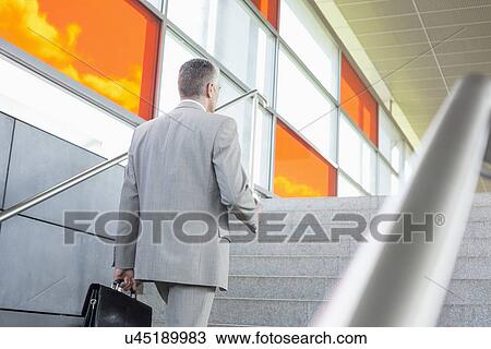 Stock Image - Rear view of middle aged businessman walking up stairs in railroad station. Fotosearch