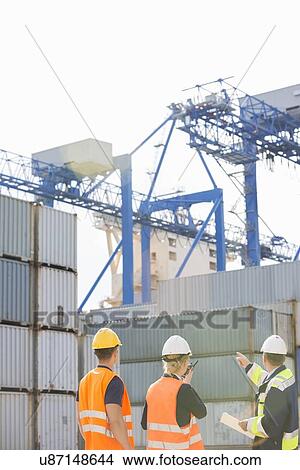 Picture - Rear view of workers inspecting cargo containers in shipping yard. Fotosearch