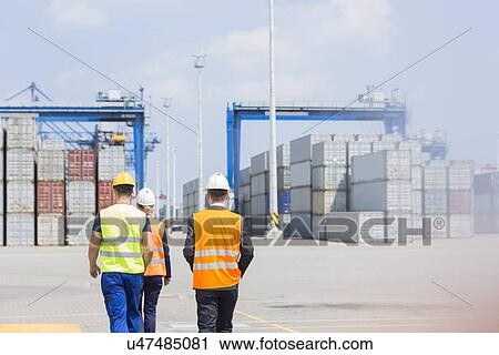 Stock Image - Rear view of workers walking in shipping yard. Fotosearch