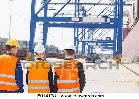 Stock Image - Rear view of workers walking in shipping yard. Fotosearch
