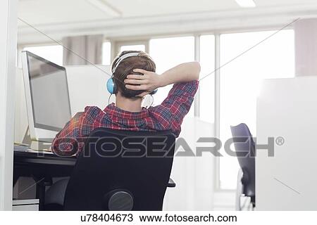 Rear view of young businessman wearing headphones at computer desk in office View Large Photo Image Stock Image - Rear view of young businessman wearing headphones at computer desk in office. Fotosearch