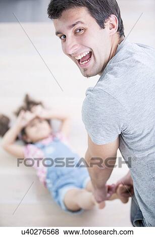 Rear view portrait of happy father dragging daughter on floor at home View Large Photo Image Stock Photo - Rear view portrait of happy father dragging daughter on floor at home. Fotosearch