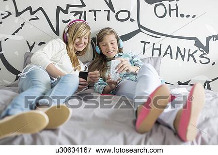 Stock Photo - Relaxed sisters listening to music at home. Fotosearch