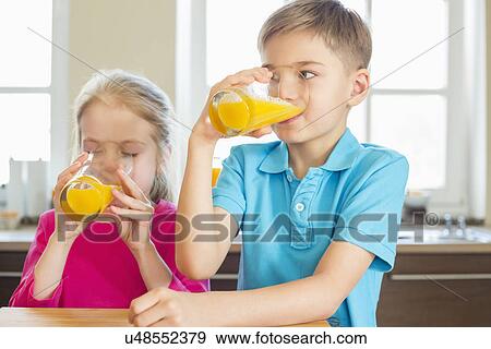 Siblings drinking orange juice in kitchen at home View Large Photo Image Stock Photo - Siblings drinking orange juice in kitchen at home. Fotosearch
