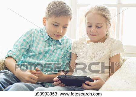 Siblings playing hand-held video game at home View Large Photo Image Stock Image - Siblings playing hand-held video game at home. Fotosearch