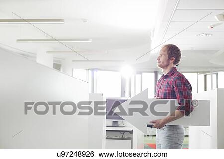 Side view of businessman holding arrow sign in creative office View Large Photo Image Stock Photograph - Side view of businessman holding arrow sign in creative office. Fotosearch