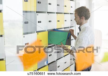 Side view of businessman putting files in locker at creative office View Large Photo Image Stock Image - Side view of businessman putting files in locker at creative office. Fotosearch