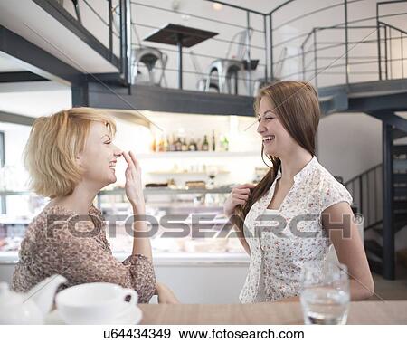 Stock Photo - Side view of cheerful young women gossiping in cafe. Fotosearch