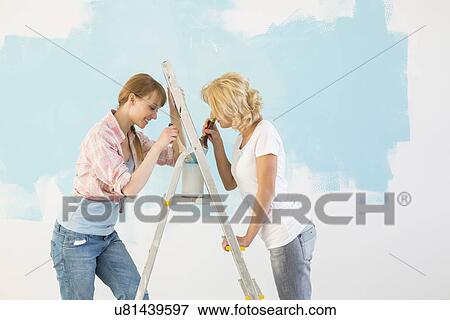 Side view of female friends painting together in new home View Large Photo Image Stock Photo - Side view of female friends painting together in new home. Fotosearch