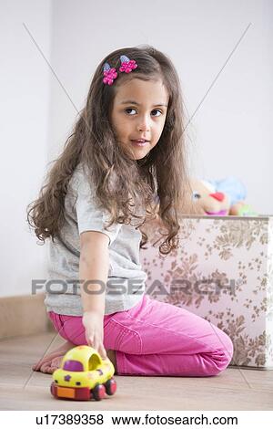 Stock Photo - Side view of girl playing with toy car at home. Fotosearch