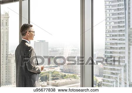 Side view of mature businessman looking through office window View Large Photo Image Stock Photo - Side view of mature businessman looking through office window. Fotosearch