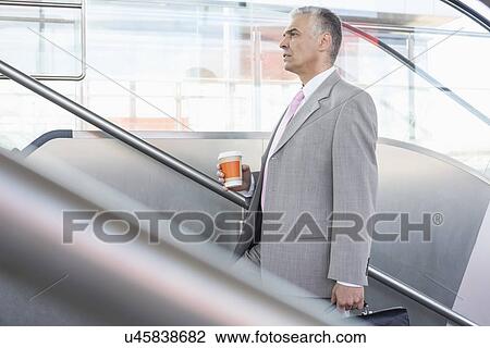 Side view of middle aged businessman with coffee cup walking up stairs in railroad station View Large Photo Image Stock Image - Side view of middle aged businessman with coffee cup walking up stairs in railroad station. Fotosearch