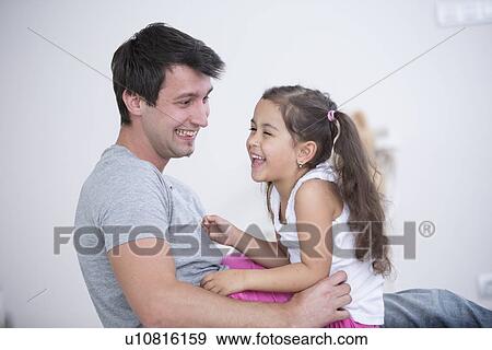 Stock Photo - Side view of playful father and daughter at home. Fotosearch