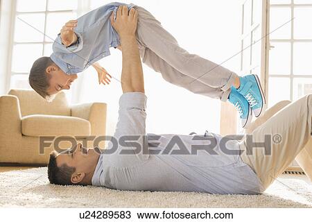 Side view of playful father lifting son while lying on floor at home View Large Photo Image Stock Image - Side view of playful father lifting son while lying on floor at home. Fotosearch