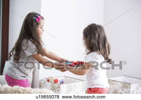 Stock Photo - Side view of sisters fighting for toy guitar at home. Fotosearch