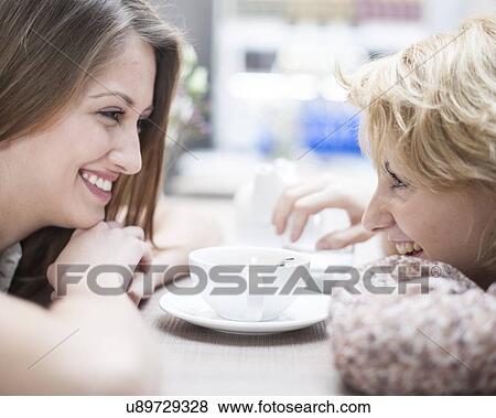 Stock Photo - Side view of smiling young female friends looking at each other in cafe. Fotosearch