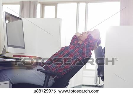Side view of young businessman relaxing at computer desk in office View Large Photo Image Stock Photography - Side view of young businessman relaxing at computer desk in office. Fotosearch