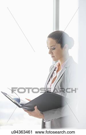 Side view of young businesswoman reading file in office View Large Photo Image Stock Image - Side view of young businesswoman reading file in office. Fotosearch