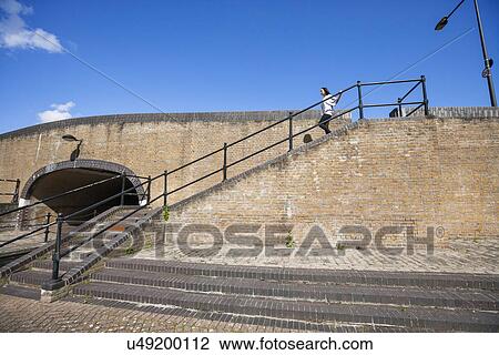 Stock Image - Side view of young woman walking down stairs against blue sky. Fotosearch