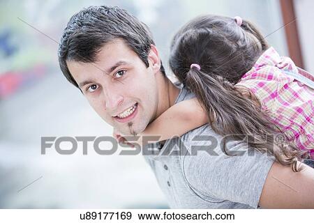 Stock Photo - Side view portrait of young man piggybacking little daughter at home. Fotosearch