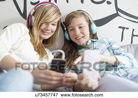 Stock Photo - Sisters listening music through headphones at home. Fotosearch