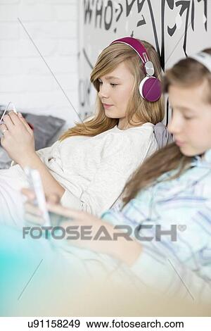Stock Photo - Sisters listening music through headphones at home. Fotosearch