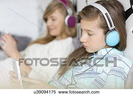 Sisters listening music through headphones at home View Large Photo Image Stock Photography - Sisters listening music through headphones at home. Fotosearch