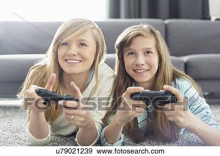 Stock Photo - Sisters playing video games in living room. Fotosearch