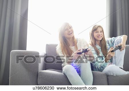Sisters playing video games on sofa View Large Photo Image Stock Image - Sisters playing video games on sofa. Fotosearch