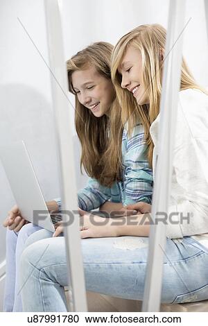 Stock Image - Sisters using laptop on stairway. Fotosearch
