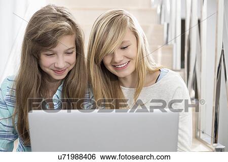 Sisters using laptop on stairway View Large Photo Image Stock Photograph - Sisters using laptop on stairway. Fotosearch