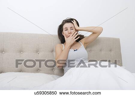 Stock Image - Sleepy woman yawning in bed. Fotosearch